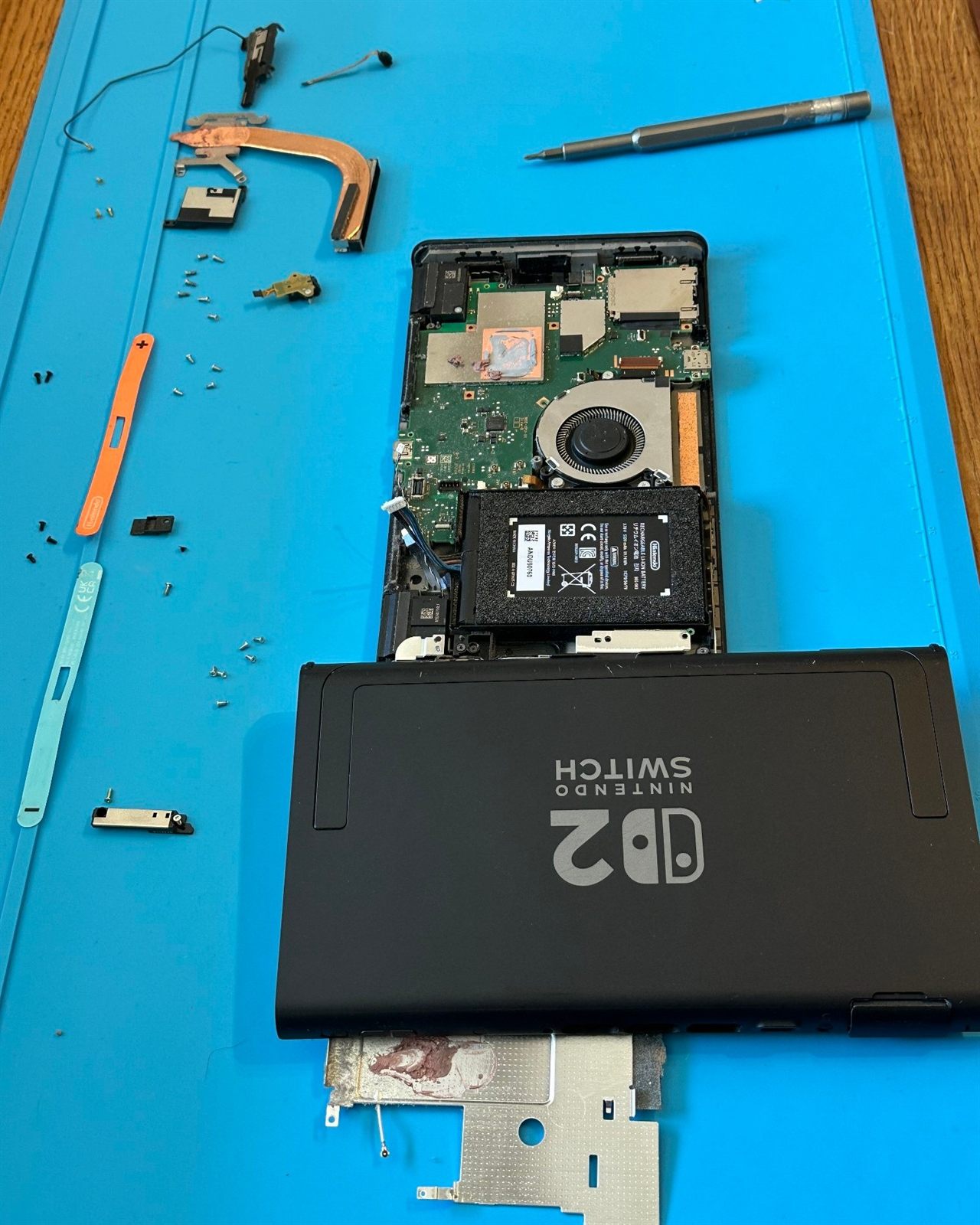 Nintendo Switch 2 ouverte sur le tapis de l'atelier : carte mère, ventilateur et batterie